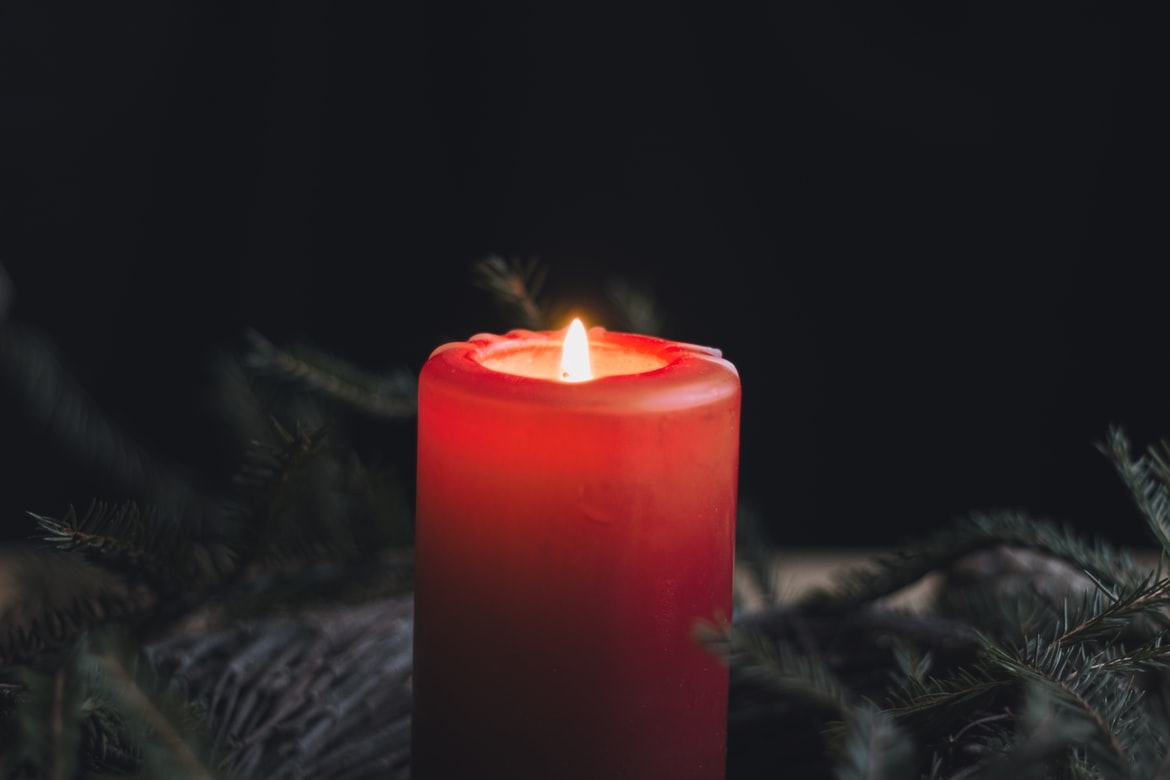 A fat red candle in the foreground of a cedar bough wreath