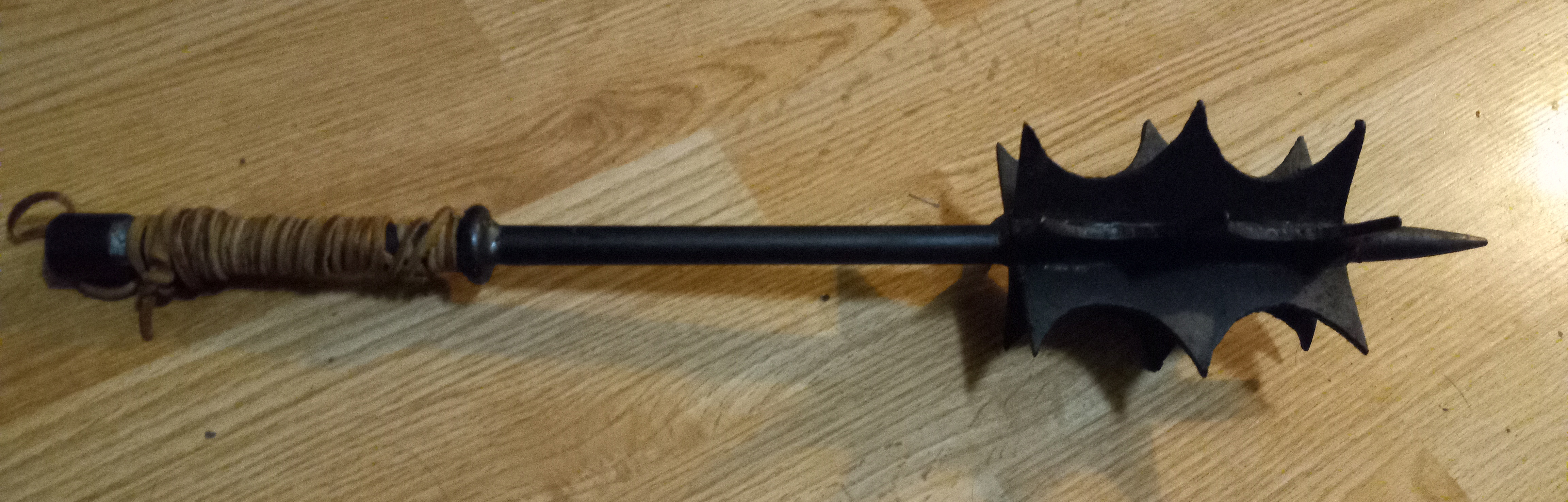 A wrought iron mace with sharp flanges against a wooden floor