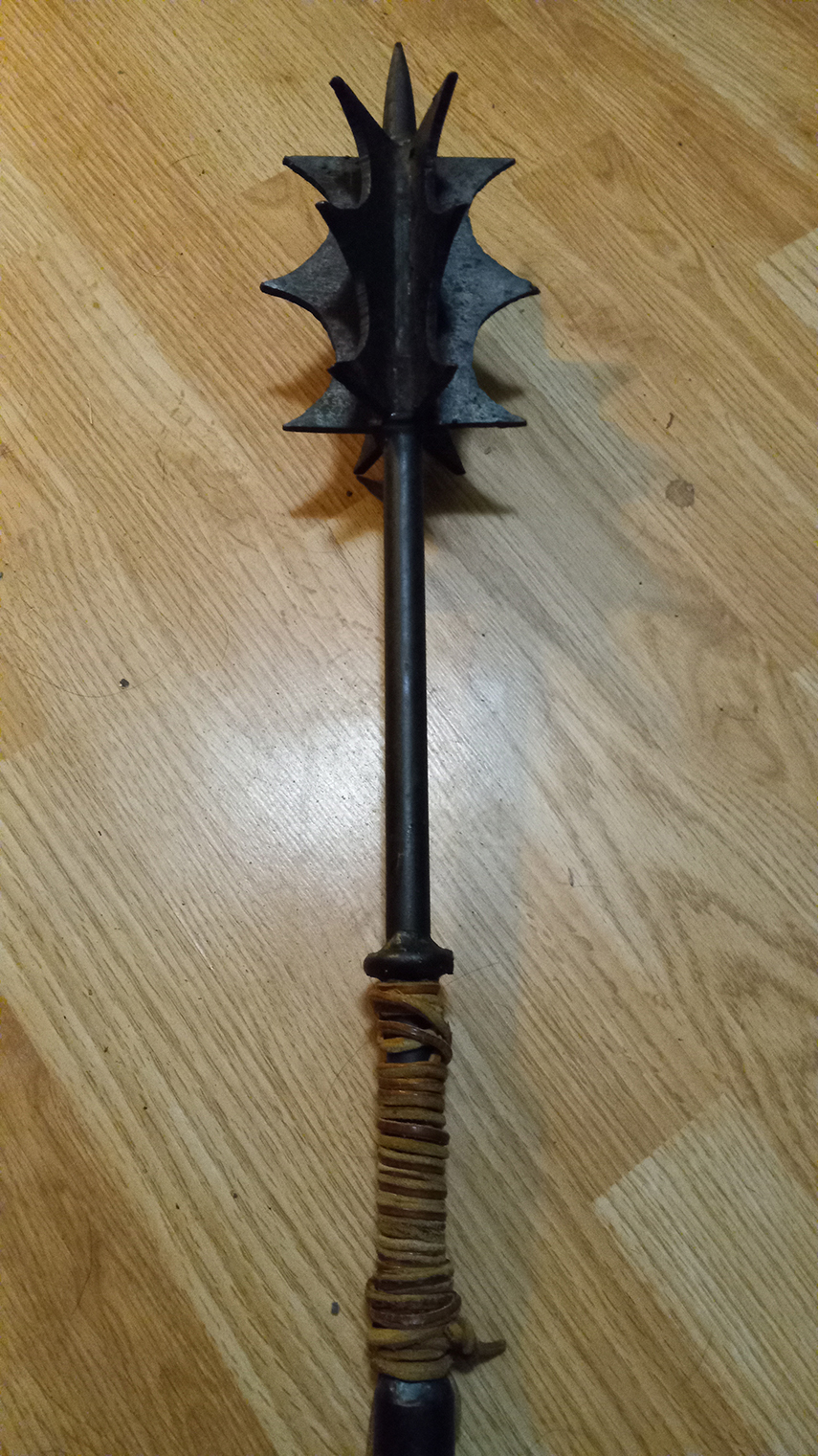 A wrought iron mace with sharp flanges and a spike against a wood floor