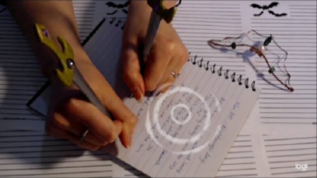 A woman writing in a spiral notebook with both hands at once using fantastical pens